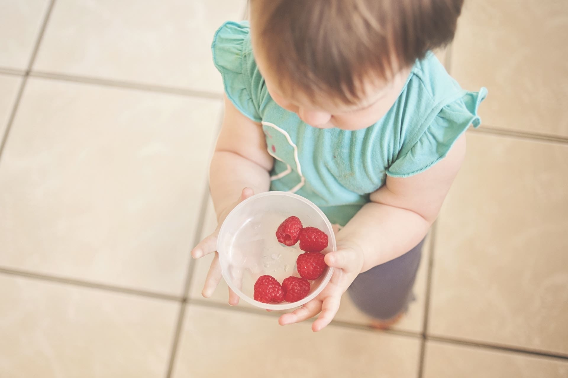 baby holding bowl of raspberries